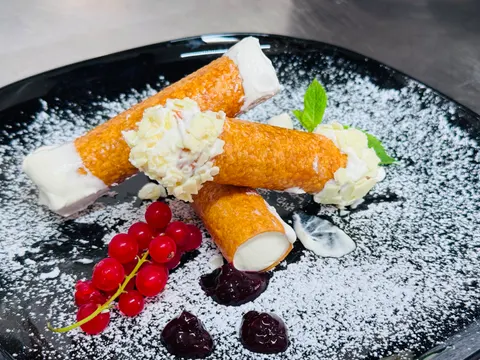 Frittierte Teigröllchen mit Sahnefüllung, weißen Schokoraspeln und Johannisbeeren